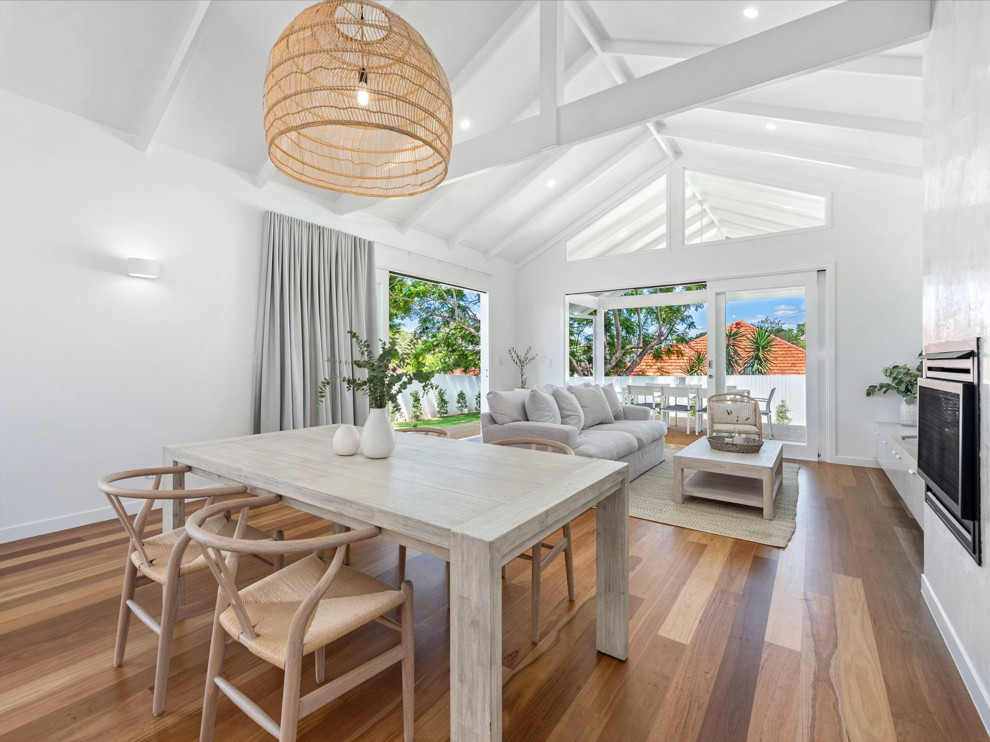 Mid-sized beach style open concept living room in Brisbane with white walls, light hardwood floors, a standard fireplace, a plaster fireplace surround, a freestanding tv, brown floor and exposed beam.