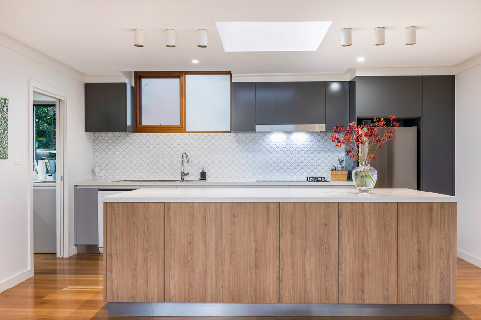 Contemporary single-wall kitchen in Canberra - Queanbeyan with an undermount sink, flat-panel cabinets, black cabinets, white splashback, stainless steel appliances, medium hardwood floors, with island, brown floor and white benchtop.