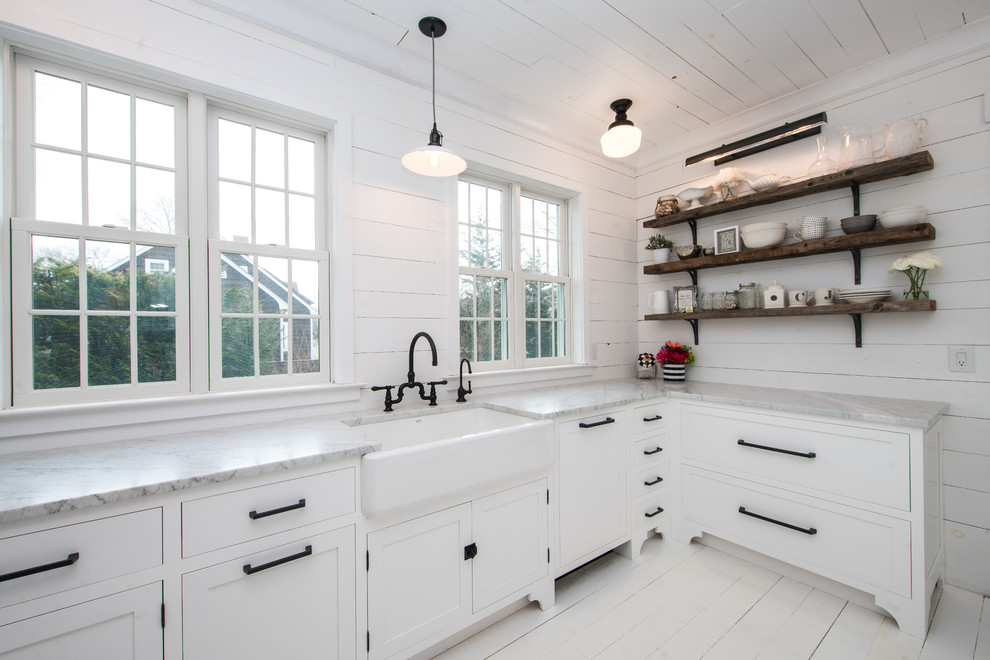 Mid-sized beach style u-shaped separate kitchen in New York with a farmhouse sink, shaker cabinets, white cabinets, marble benchtops, white splashback, timber splashback, panelled appliances, painted wood floors, no island and white floor.