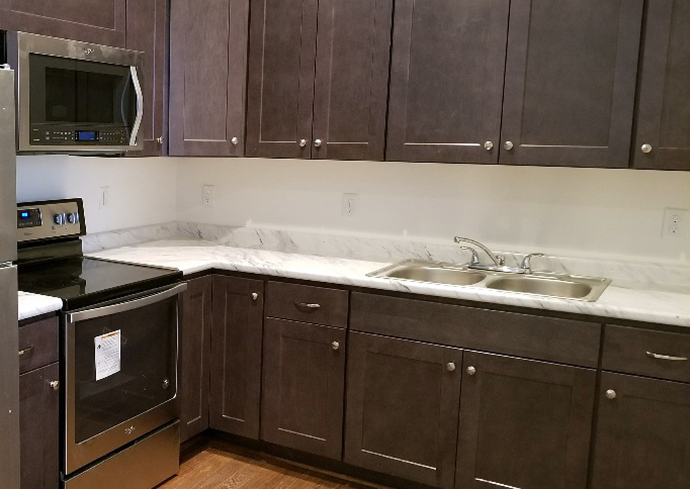 Example of a small transitional l-shaped dark wood floor and brown floor kitchen design with a double-bowl sink, recessed-panel cabinets, dark wood cabinets, laminate countertops, white backsplash, stainless steel appliances and white countertops