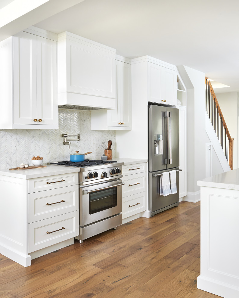 Inspiration for a transitional galley kitchen in Toronto with recessed-panel cabinets, white cabinets, white splashback, mosaic tile splashback, stainless steel appliances, medium hardwood floors, brown floor and white benchtop.