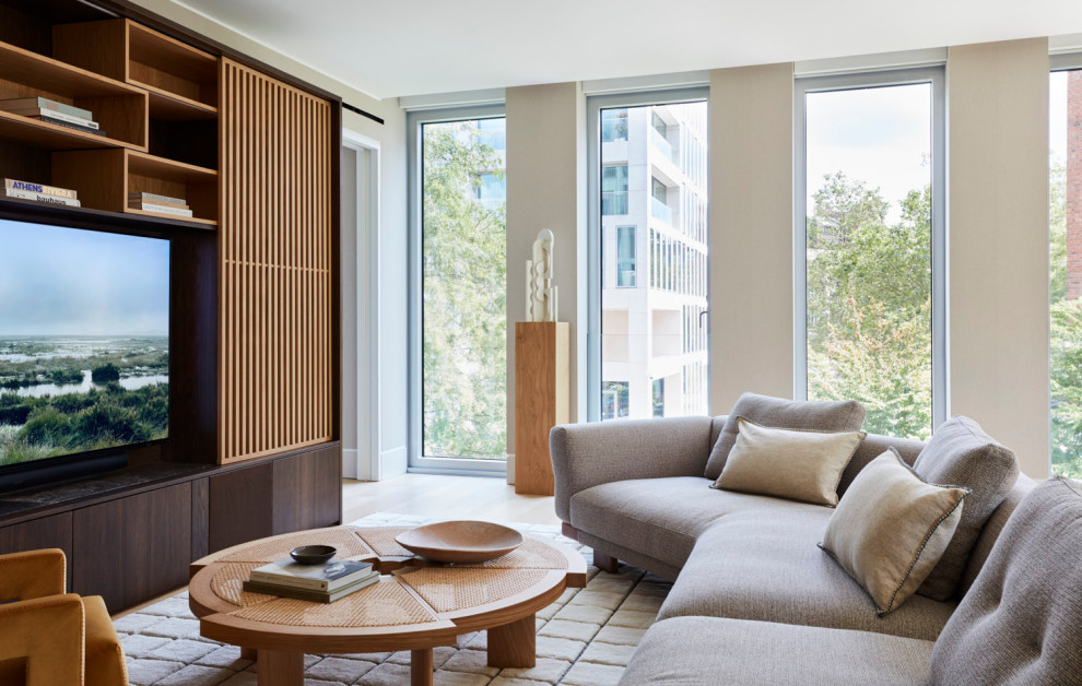 Imagen de salón abierto de tamaño medio con paredes beige, suelo de madera clara y televisor retractable