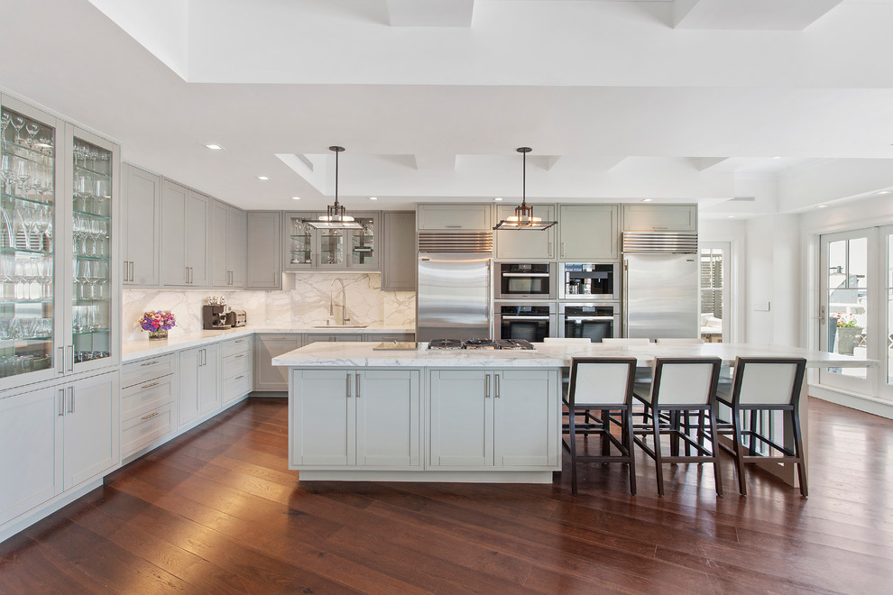 This is an example of a transitional l-shaped kitchen in New York with an undermount sink, shaker cabinets, grey cabinets, white splashback, stone slab splashback, stainless steel appliances, dark hardwood floors and with island.