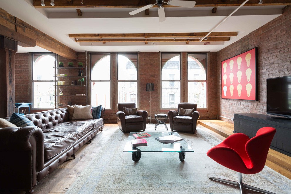 Photo of an industrial open concept living room in New York with medium hardwood floors, a freestanding tv and brown floor.