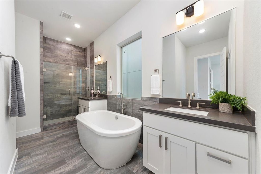 Photo of a medium sized contemporary ensuite bathroom in Houston with shaker cabinets, white cabinets, a freestanding bath, an alcove shower, brown tiles, grey tiles, porcelain tiles, white walls, porcelain flooring, a submerged sink, engineered stone worktops, grey floors, a hinged door and grey worktops.