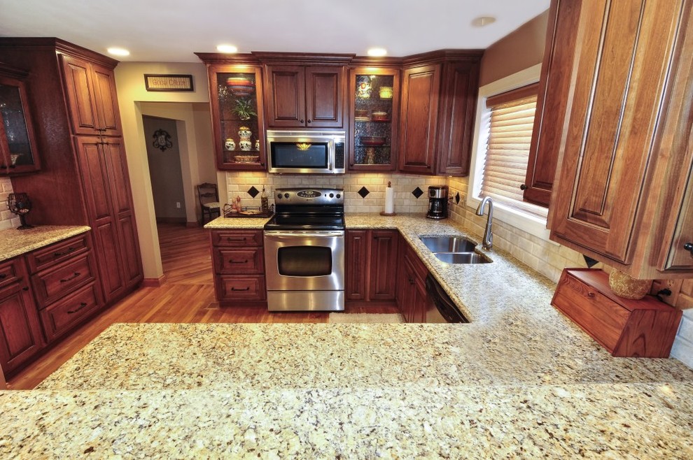 Transitional u-shaped eat-in kitchen photo in St Louis with an undermount sink, raised-panel cabinets, dark wood cabinets, granite countertops, beige backsplash, subway tile backsplash and stainless steel appliances