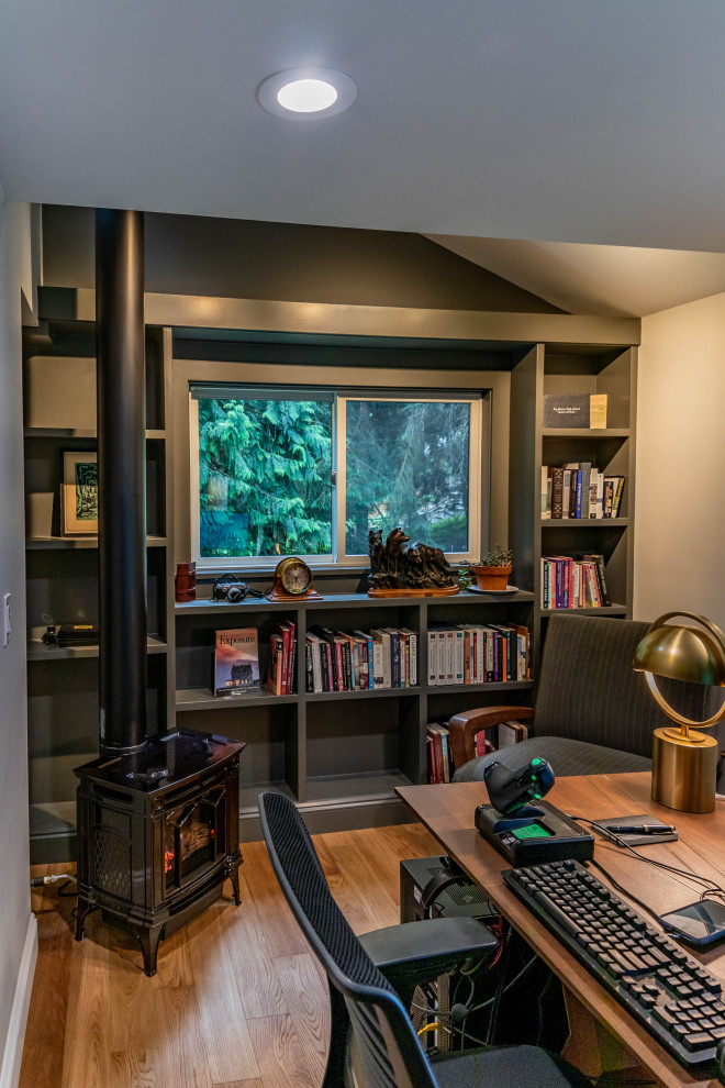 Design ideas for a mid-sized contemporary home office in Seattle with a library, grey walls, light hardwood floors, a wood stove, a metal fireplace surround, a freestanding desk and brown floor.