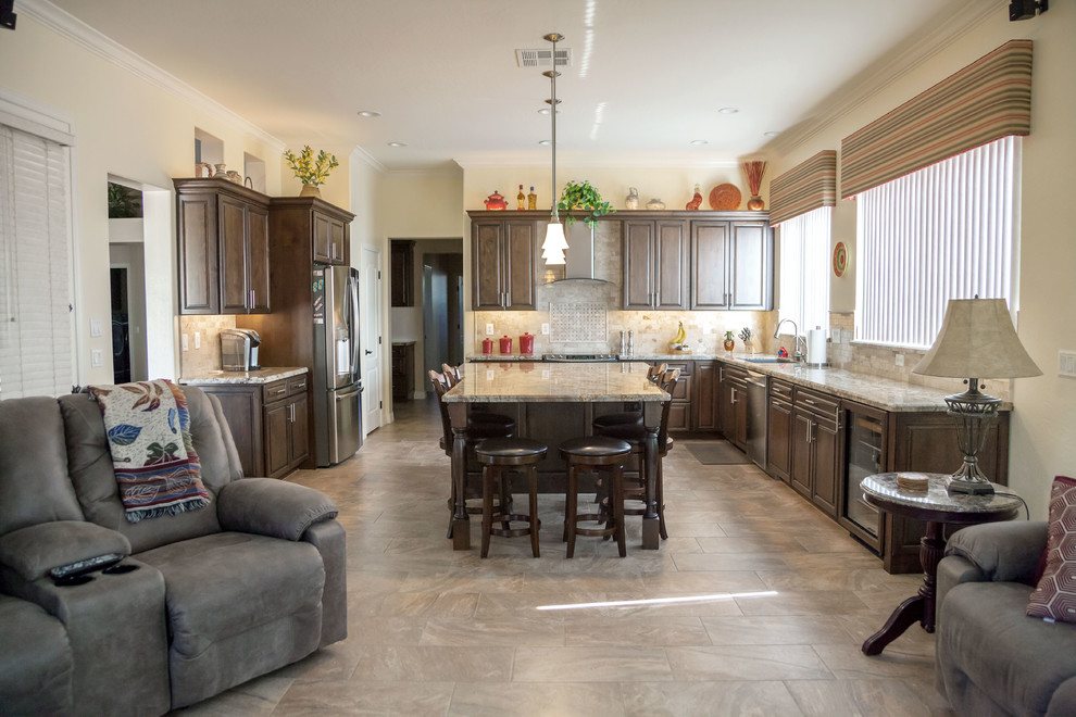 Open concept kitchen - transitional galley porcelain tile open concept kitchen idea in Phoenix with an undermount sink, raised-panel cabinets, dark wood cabinets, granite countertops, beige backsplash, stone tile backsplash, stainless steel appliances and an island