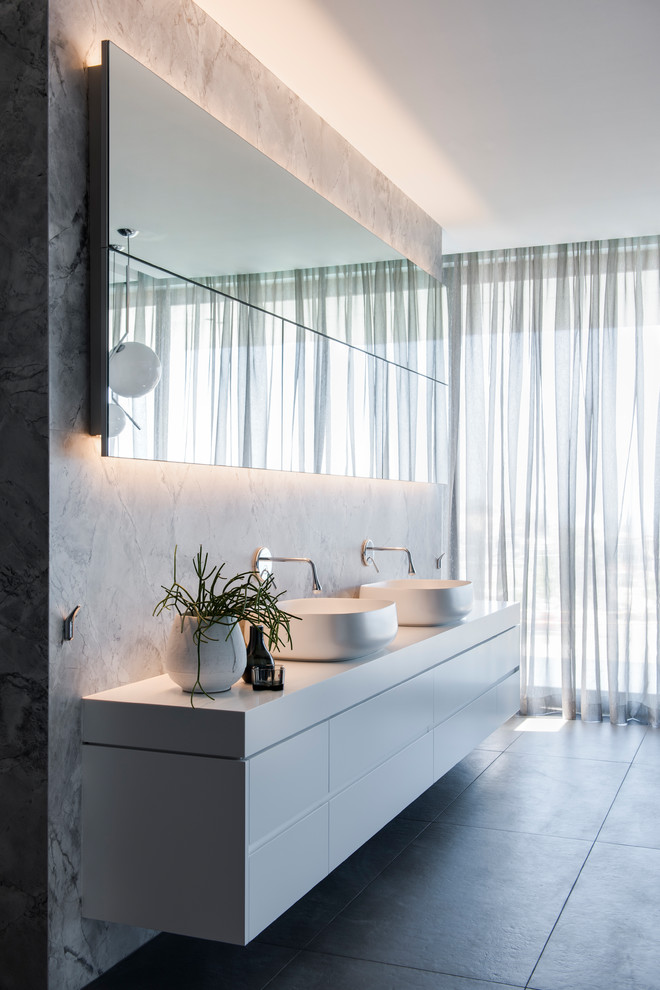 Large contemporary master bathroom in Sydney with white cabinets, a freestanding tub, an open shower, a wall-mount toilet, gray tile, marble, grey walls, porcelain floors, a vessel sink, solid surface benchtops, grey floor, an open shower, white benchtops and flat-panel cabinets.