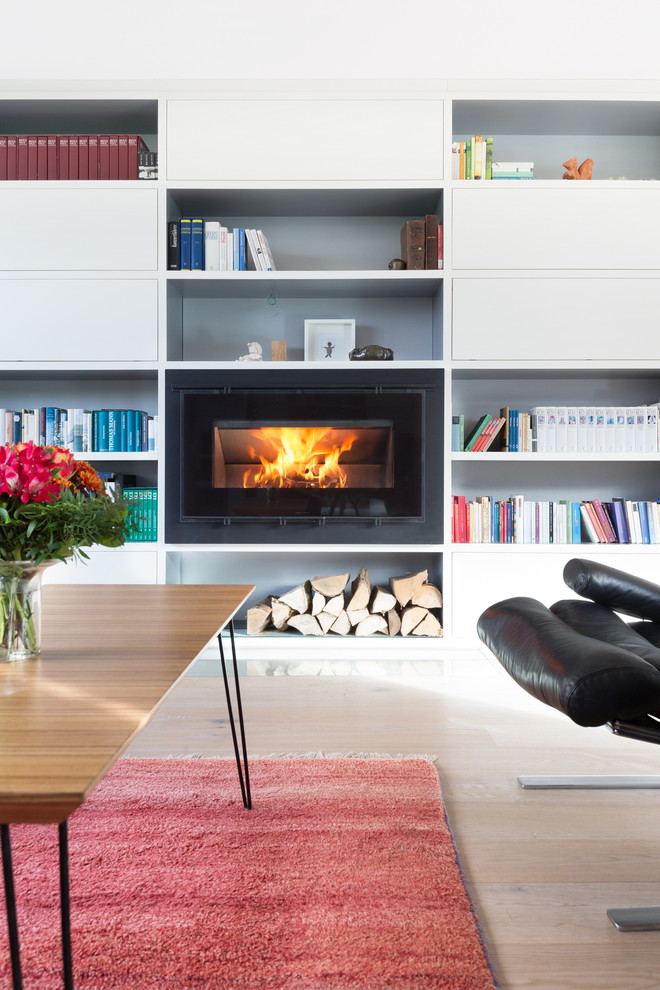 This is an example of a modern living room in Cologne with a library, white walls, painted wood floors, a wood stove and a metal fireplace surround.