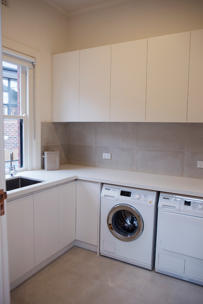 Photo of a small contemporary l-shaped dedicated laundry room in Melbourne with an undermount sink, white cabinets, quartz benchtops, a side-by-side washer and dryer, flat-panel cabinets, white walls and concrete floors.