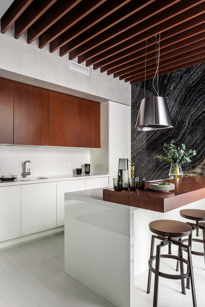 Photo of a contemporary galley kitchen in Moscow with an integrated sink, flat-panel cabinets, dark wood cabinets, panelled appliances, light hardwood floors, a peninsula and white benchtop.