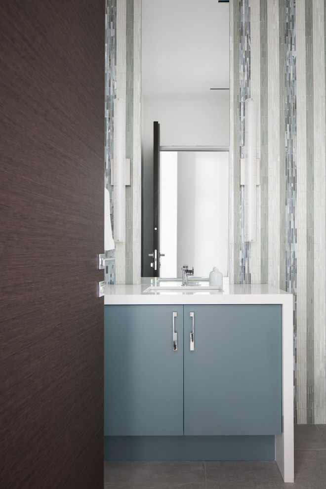 Photo of a medium sized contemporary cloakroom in Tampa with flat-panel cabinets, green cabinets, a one-piece toilet, multi-coloured tiles, glass tiles, multi-coloured walls, porcelain flooring, a submerged sink, engineered stone worktops, grey floors, white worktops and a built in vanity unit.