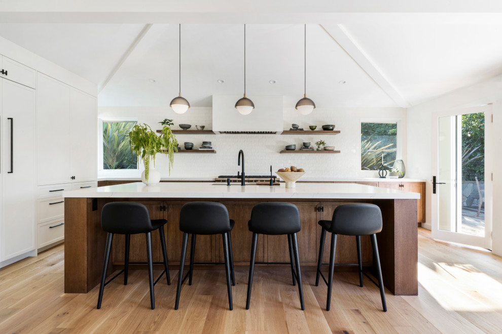 Photo of a beach style eat-in kitchen in San Francisco with an undermount sink, flat-panel cabinets, white cabinets, quartz benchtops, white splashback, ceramic splashback, stainless steel appliances, light hardwood floors, with island and white benchtop.