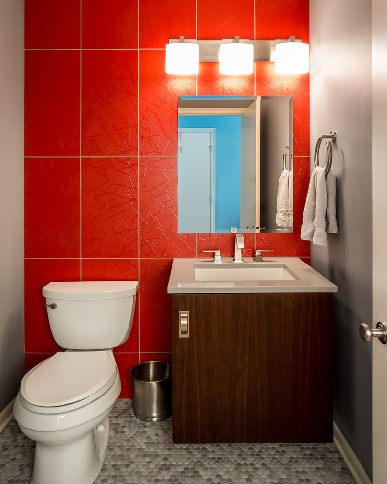 This is an example of a mid-sized contemporary powder room in Minneapolis with an undermount sink, flat-panel cabinets, dark wood cabinets, solid surface benchtops, a two-piece toilet, red tile, porcelain tile, red walls and grey benchtops.