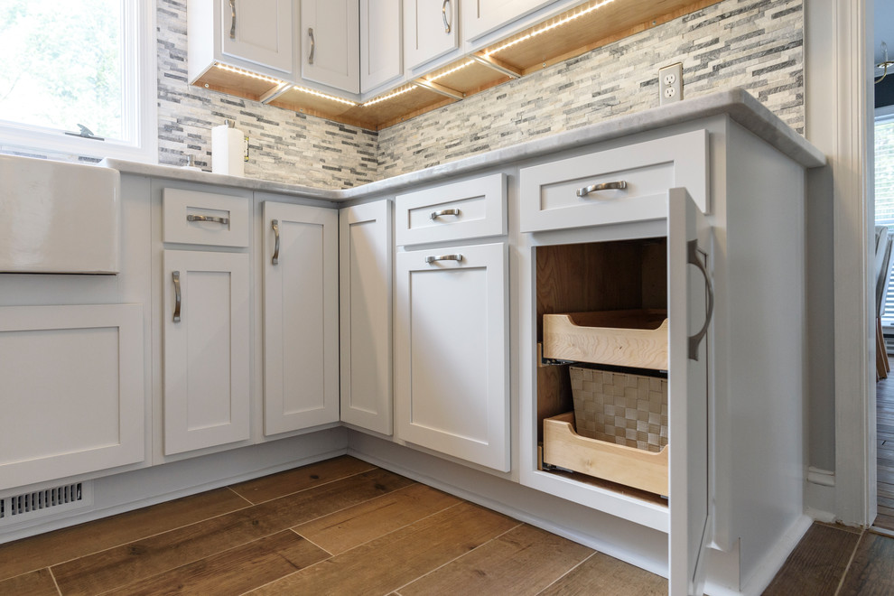 Example of a large transitional l-shaped ceramic tile and brown floor eat-in kitchen design in Baltimore with a farmhouse sink, shaker cabinets, white cabinets, granite countertops, gray backsplash, stone tile backsplash, stainless steel appliances, no island and white countertops