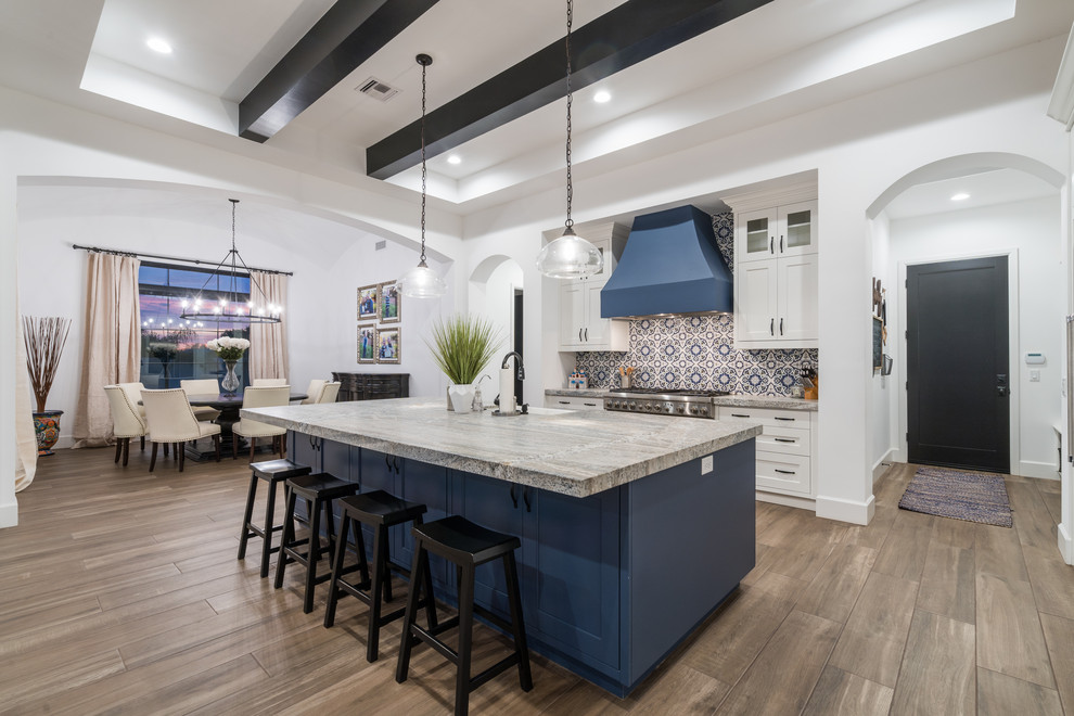 Inspiration for a transitional l-shaped eat-in kitchen in Phoenix with a farmhouse sink, shaker cabinets, white cabinets, multi-coloured splashback, stainless steel appliances, medium hardwood floors, with island, brown floor and grey benchtop.