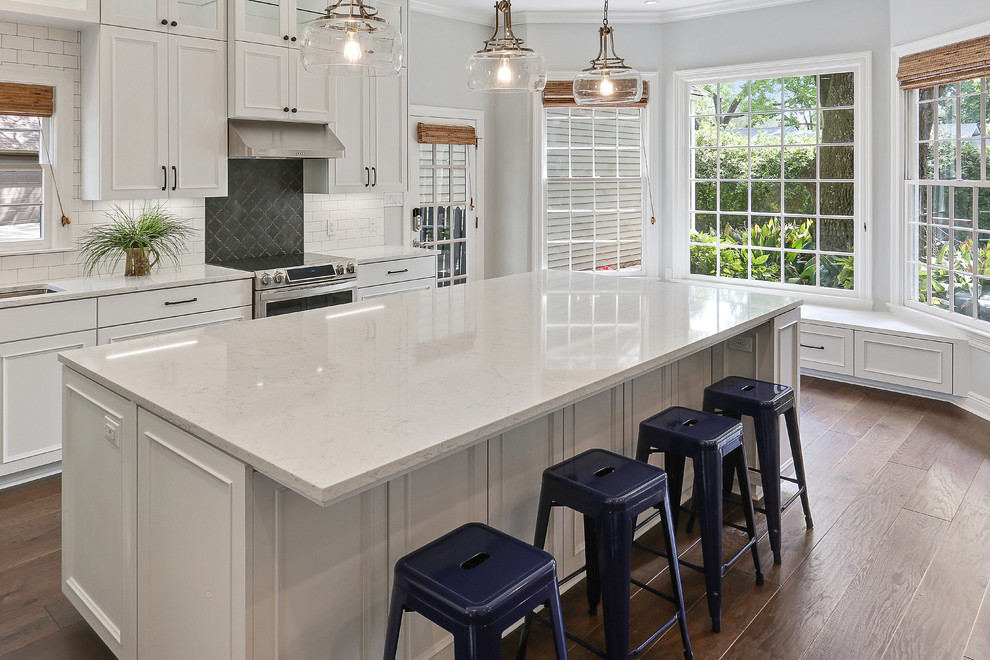 Design ideas for a mid-sized transitional l-shaped open plan kitchen in New Orleans with an undermount sink, white cabinets, quartz benchtops, white splashback, subway tile splashback, stainless steel appliances, with island, brown floor, white benchtop, recessed-panel cabinets and medium hardwood floors.