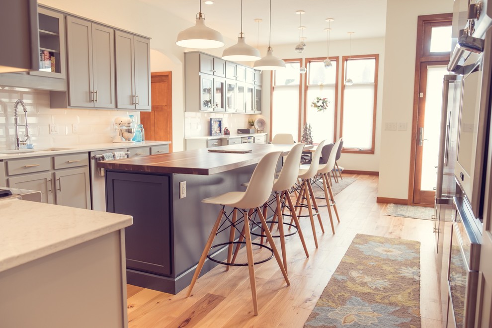 Inspiration for a large transitional l-shaped eat-in kitchen in Cedar Rapids with a single-bowl sink, shaker cabinets, grey cabinets, marble benchtops, white splashback, subway tile splashback, stainless steel appliances, light hardwood floors, with island and brown floor.