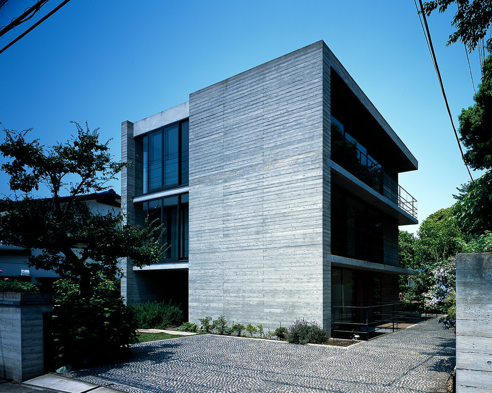 Large asian three-storey concrete grey house exterior in Yokohama with a flat roof.