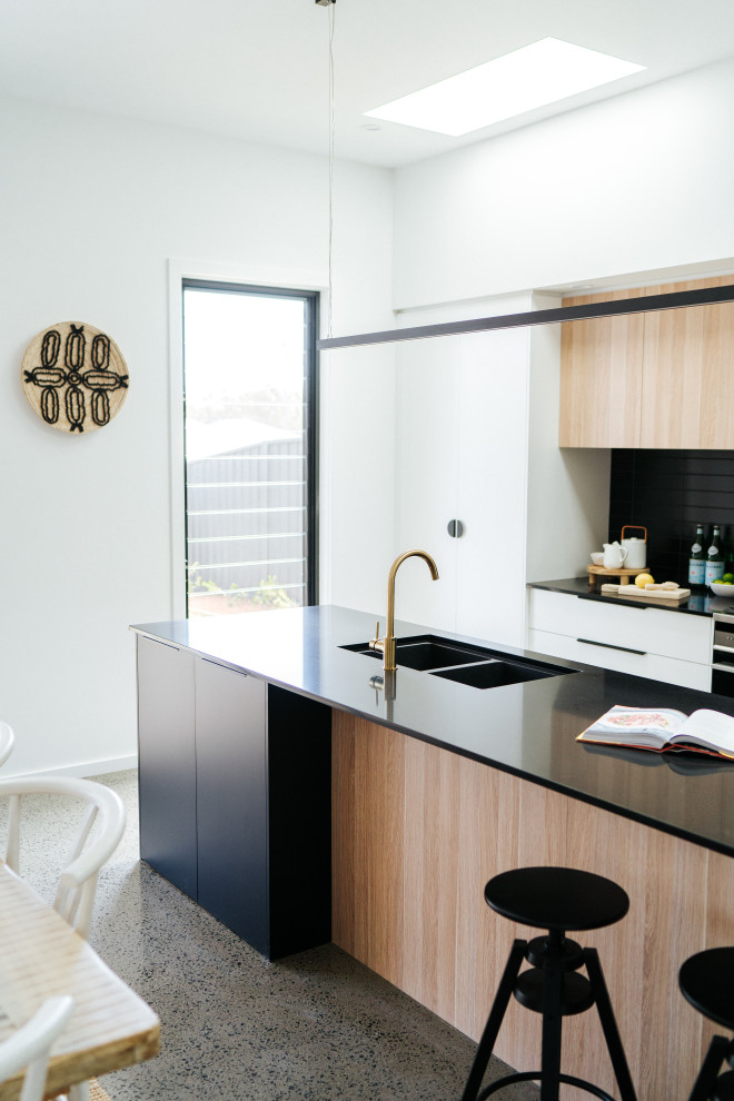 Inspiration for a mid-sized modern galley open plan kitchen in Wollongong with an undermount sink, flat-panel cabinets, black cabinets, quartz benchtops, black splashback, ceramic splashback, stainless steel appliances, concrete floors, with island, grey floor and black benchtop.