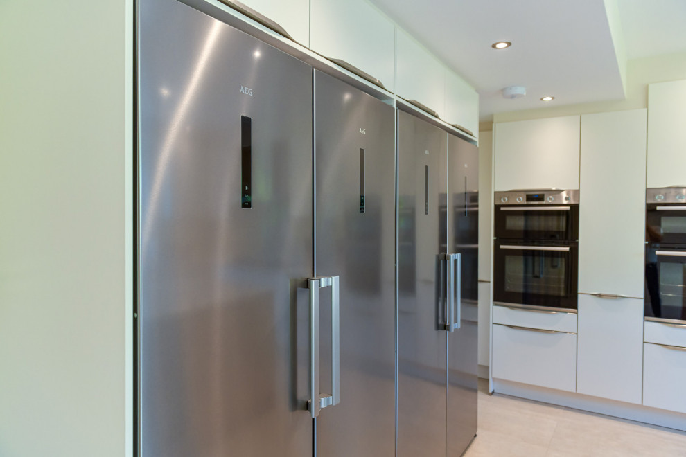 Photo of a large modern l-shaped open plan kitchen in London with a double-bowl sink, shaker cabinets, white cabinets, limestone benchtops, grey splashback, slate splashback, stainless steel appliances, with island and white benchtop.