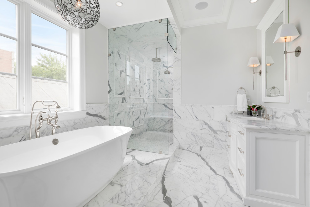 Photo of a large transitional master bathroom in Chicago with an undermount sink, beaded inset cabinets, white cabinets, marble benchtops, a freestanding tub, an alcove shower, a two-piece toilet, white tile, stone tile, grey walls and marble floors.