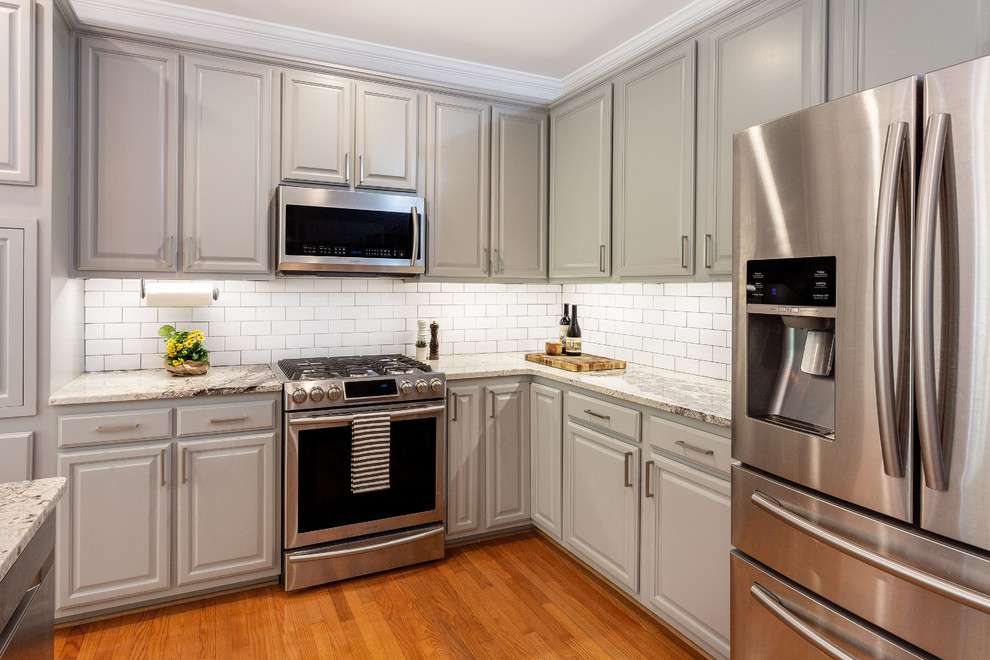 Example of a mid-sized transitional l-shaped medium tone wood floor eat-in kitchen design in Richmond with a farmhouse sink, gray cabinets, granite countertops, white backsplash, ceramic backsplash, stainless steel appliances, an island and multicolored countertops