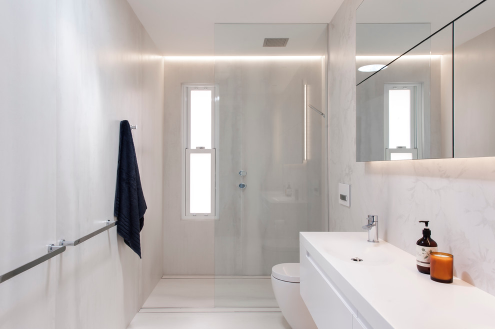 Mid-sized modern bathroom in Sydney with an integrated sink, solid surface benchtops, an open shower, a wall-mount toilet, beige tile, porcelain tile, beige walls, porcelain floors and an open shower.