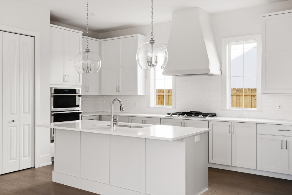 Inspiration for a large transitional medium tone wood floor and brown floor kitchen pantry remodel in Orlando with an undermount sink, shaker cabinets, white cabinets, marble countertops, white backsplash, porcelain backsplash, stainless steel appliances, an island and white countertops