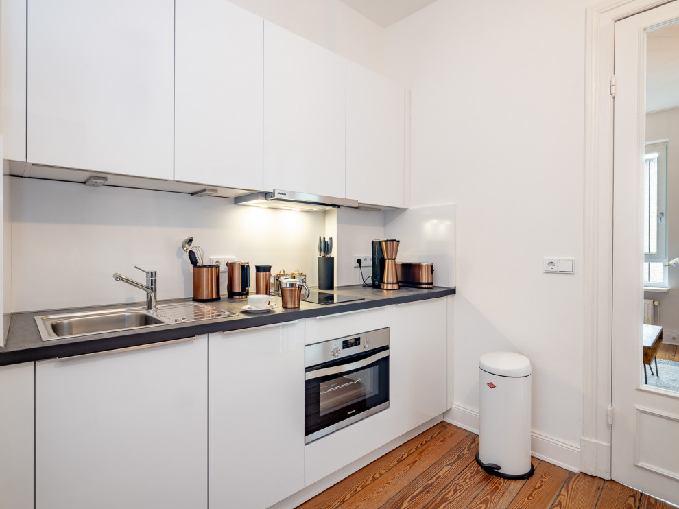 This is an example of a small mediterranean single-wall eat-in kitchen in Other with a single-bowl sink, white cabinets, solid surface benchtops, white splashback, stainless steel appliances, painted wood floors, no island and black benchtop.