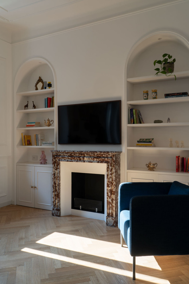 Стильный дизайн: большая открытая гостиная комната в классическом стиле с с книжными шкафами и полками, белыми стенами, светлым паркетным полом, фасадом камина из камня и телевизором на стене - последний тренд