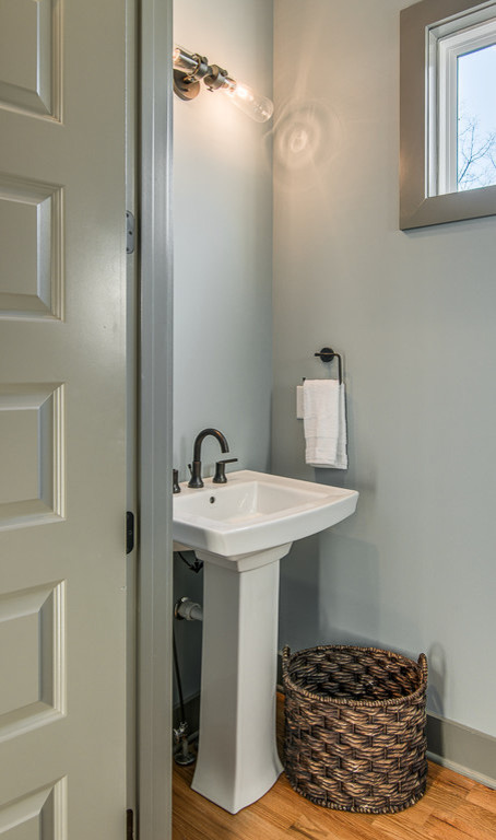 Small arts and crafts powder room in Nashville with blue walls, light hardwood floors and a pedestal sink.