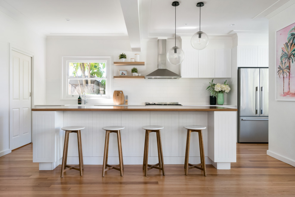 Design ideas for a beach style open plan kitchen in Sydney with a farmhouse sink, white cabinets, wood benchtops, white splashback, subway tile splashback, stainless steel appliances and with island.