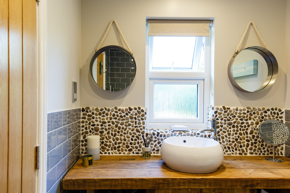 This is an example of a beach style master wet room bathroom in Cambridgeshire with furniture-like cabinets, dark wood cabinets, a one-piece toilet, gray tile, subway tile, grey walls, ceramic floors, a drop-in sink, wood benchtops and an open shower.