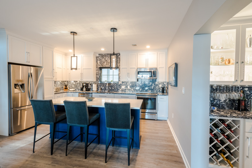 Mid-sized industrial l-shaped eat-in kitchen in Baltimore with an undermount sink, white cabinets, quartz benchtops, blue splashback, engineered quartz splashback, stainless steel appliances, vinyl floors, with island, brown floor and blue benchtop.