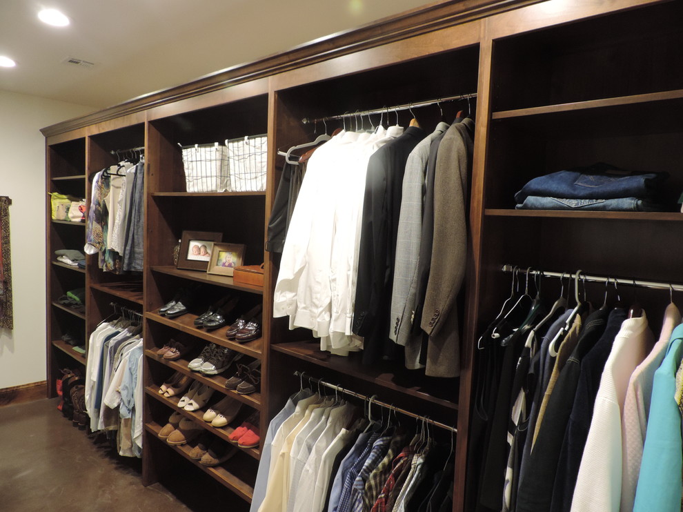This is an example of a mid-sized traditional gender-neutral walk-in wardrobe in Kansas City with open cabinets, brown cabinets and concrete floors.