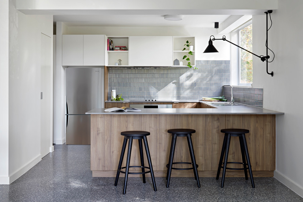 Photo of a contemporary u-shaped kitchen in Melbourne with a drop-in sink, flat-panel cabinets, medium wood cabinets, blue splashback, mosaic tile splashback, stainless steel appliances, a peninsula, grey floor and grey benchtop.