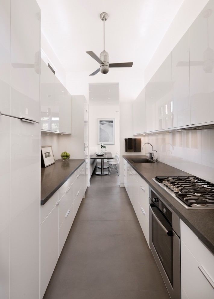 Design ideas for a contemporary kitchen in Santa Barbara with a single-bowl sink, flat-panel cabinets, white cabinets, glass sheet splashback, stainless steel appliances and concrete floors.