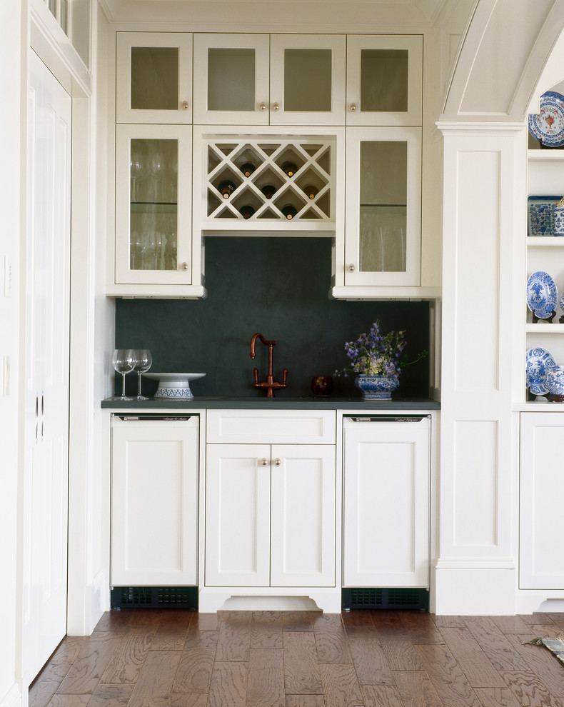 This is an example of a mid-sized traditional single-wall wet bar in Providence with white cabinets, glass-front cabinets, green splashback, brown floor and dark hardwood floors.