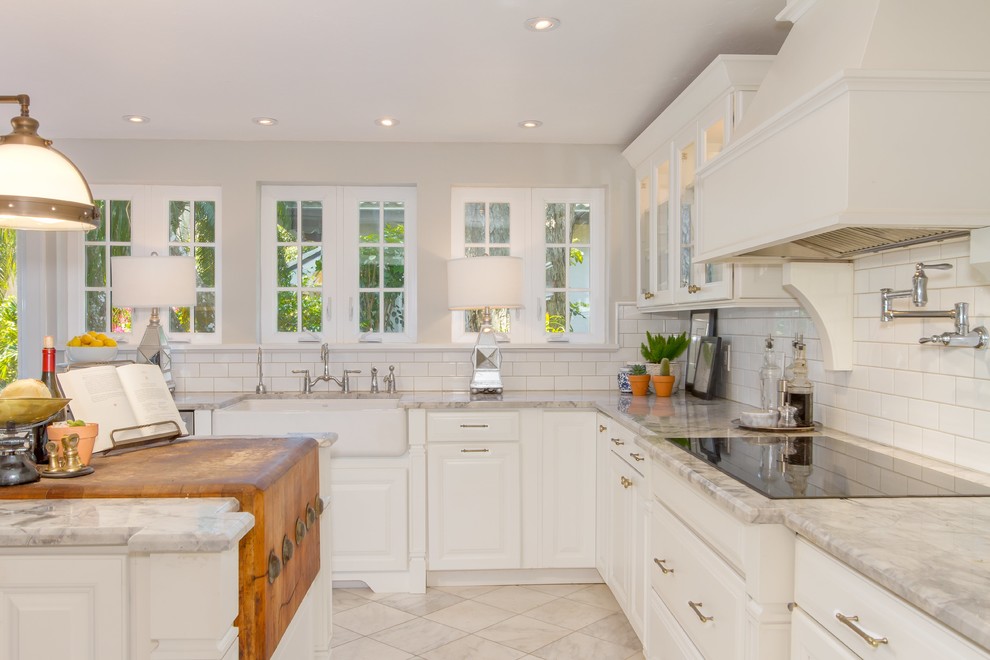 Example of a mid-sized transitional u-shaped porcelain tile and white floor open concept kitchen design in Miami with a farmhouse sink, raised-panel cabinets, white cabinets, marble countertops, white backsplash, subway tile backsplash, stainless steel appliances and an island