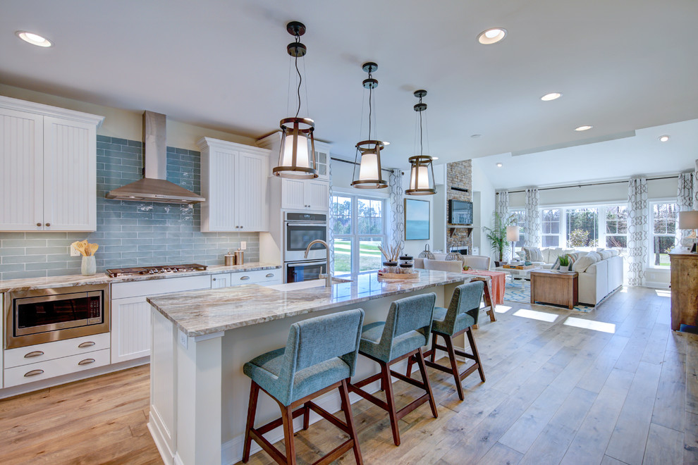 Design ideas for a transitional l-shaped open plan kitchen in Baltimore with a farmhouse sink, white cabinets, blue splashback, subway tile splashback, stainless steel appliances, medium hardwood floors, with island, brown floor, grey benchtop and recessed-panel cabinets.