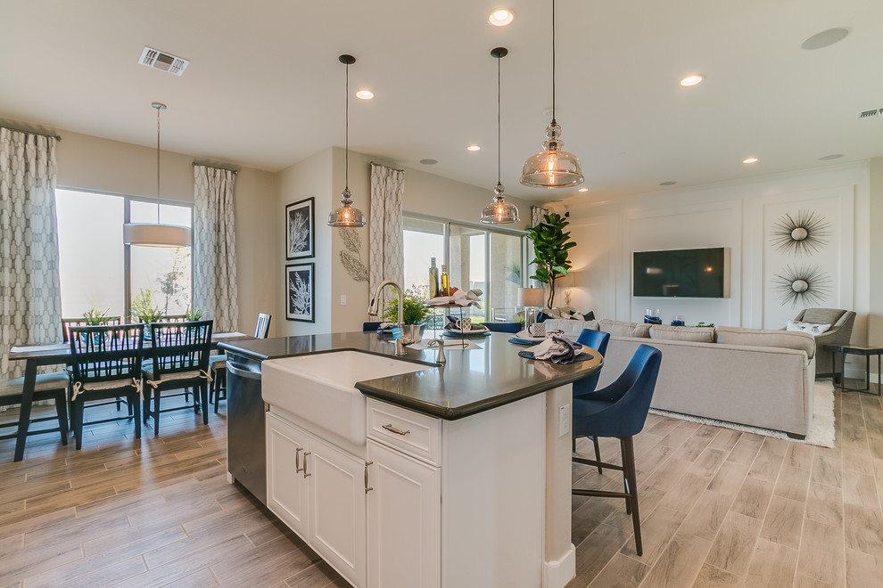 This is an example of a large contemporary l-shaped eat-in kitchen in Phoenix with a farmhouse sink, recessed-panel cabinets, white cabinets, solid surface benchtops, beige splashback, ceramic splashback, stainless steel appliances, ceramic floors, with island and beige floor.