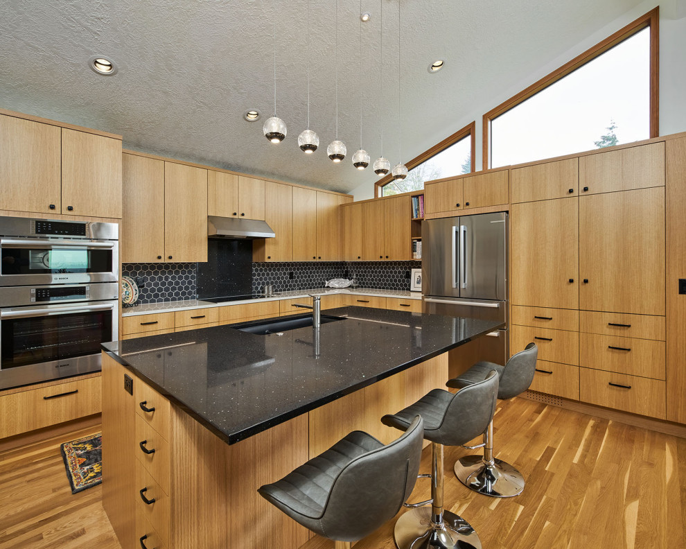 Large trendy l-shaped medium tone wood floor, brown floor and vaulted ceiling open concept kitchen photo in Portland with an undermount sink, flat-panel cabinets, light wood cabinets, quartz countertops, black backsplash, porcelain backsplash, stainless steel appliances, an island and multicolored countertops