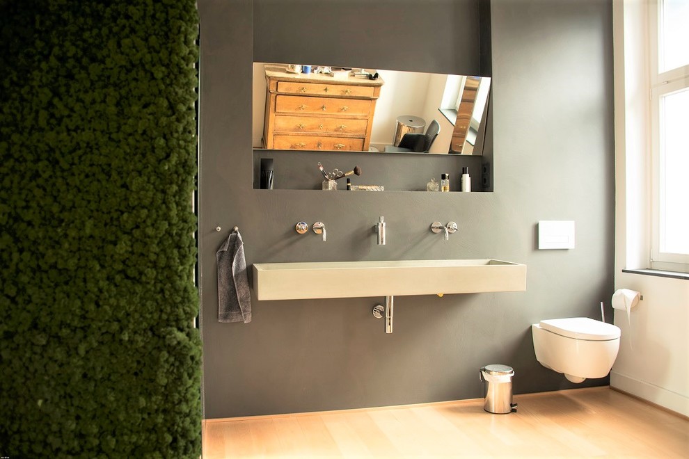 This is an example of a mid-sized contemporary 3/4 bathroom in Bonn with grey walls, light hardwood floors, concrete benchtops, an open shower, open cabinets, a freestanding tub, an open shower, a wall-mount toilet, gray tile, a console sink and brown floor.