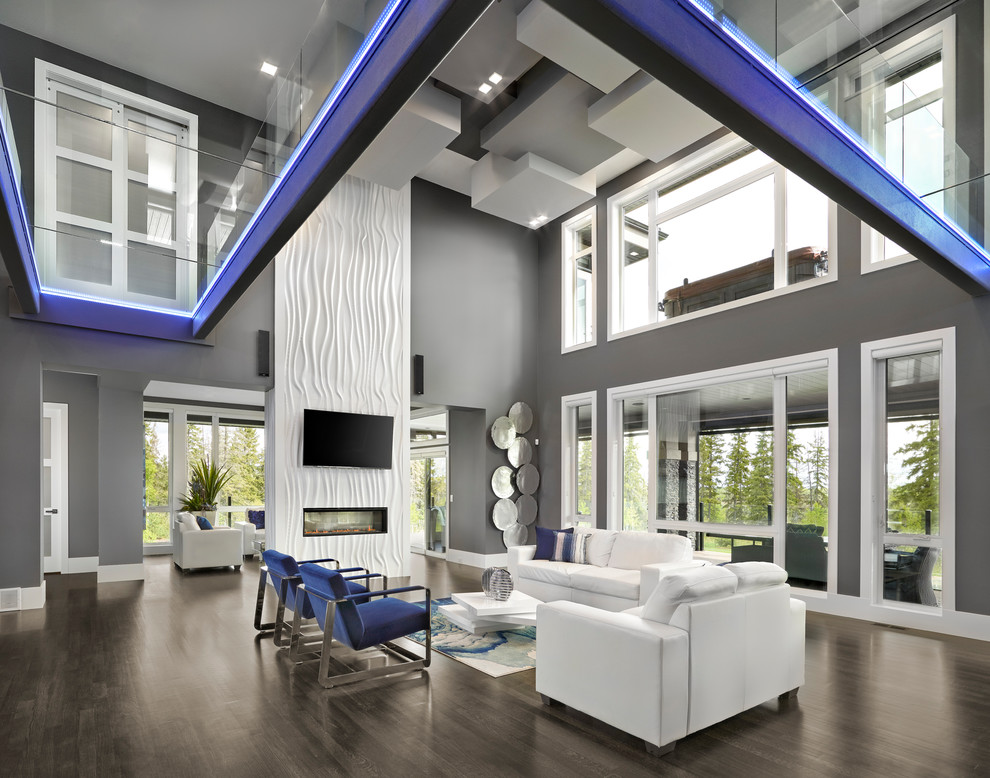 Expansive contemporary open concept family room in Edmonton with grey walls, dark hardwood floors, a two-sided fireplace, a plaster fireplace surround, a wall-mounted tv and brown floor.