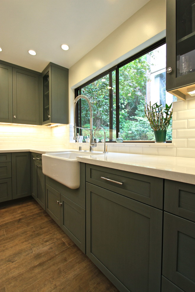 Inspiration for a mid-sized transitional u-shaped open plan kitchen in Los Angeles with a farmhouse sink, recessed-panel cabinets, green cabinets, marble benchtops, white splashback, ceramic splashback, stainless steel appliances, porcelain floors and with island.