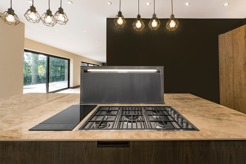 Mid-sized contemporary l-shaped open plan kitchen in London with glass benchtops, multi-coloured splashback, glass sheet splashback, with island and beige benchtop.