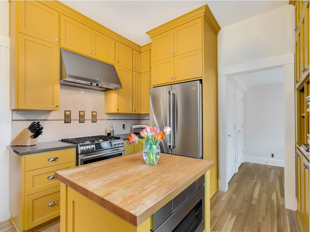 Inspiration for a large arts and crafts u-shaped separate kitchen in Portland with a farmhouse sink, shaker cabinets, yellow cabinets, quartz benchtops, multi-coloured splashback, subway tile splashback, stainless steel appliances, light hardwood floors, with island and grey benchtop.