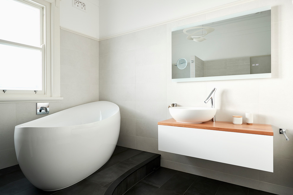 Photo of a contemporary master bathroom in Sydney with white cabinets, a freestanding tub, a two-piece toilet, beige walls and wood benchtops.
